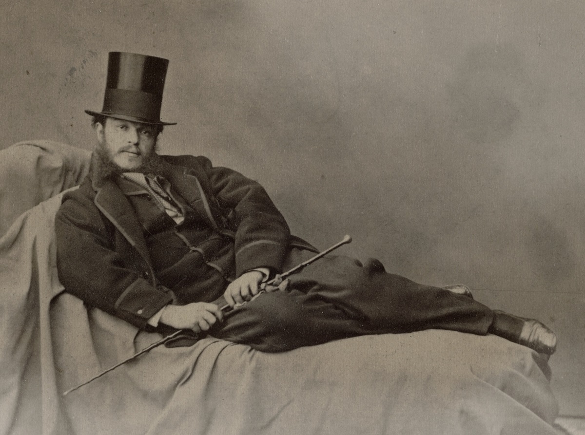 A big man in a tophat reclines on a sofa